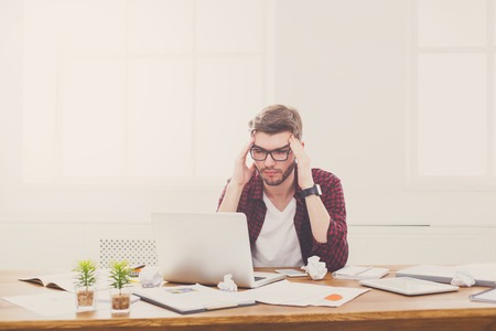 Young stressed and unhappy businessman with laptop in modern white office interior. Job problems...