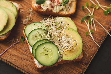 Green vegetables morning sandwiches with micro greens. Fresh avocado and cucumber toasts with cream cheese. Healthy breakfast on wooden board closeupの写真素材