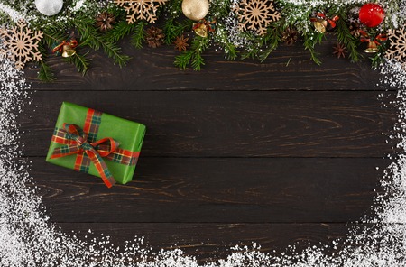 Christmas background with decorations, green gift box and garland frame, top view on wooden table surface with copy space. Christmas ornaments and present surrounded by snow. Winter holidays concept.の写真素材