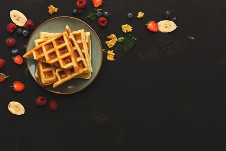 Belgian waffles with berries and fruits on black background. Border of checkered biscuits top view with copy space. Sweet food and tasty breakfast conceptの写真素材