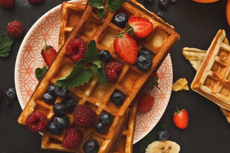Belgian waffles with berries and fruits on black background. Top view on checkered biscuits. Sweet food and tasty breakfast conceptの写真素材