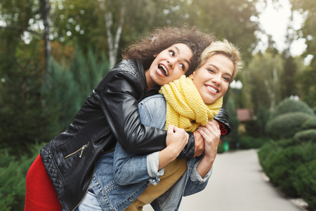 Outdoors portrait of two female multiethnic friends. Girls in casual warm outfits having a walk in city park in cold season and having fun, copy space. Urban lifestyle, friendship conceptの写真素材