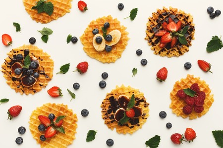 Belgian waffles with fruits and caramel on white background. Assortment of checkered biscuit with banana, blueberry, strawberry and topping. Sweet food and tasty breakfast concept, top viewの写真素材