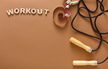 Workout word, jumping rope and measuring tape on brown background. Skipping rope, sport supply, weightloss, slimming conceptの写真素材