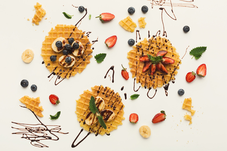 Belgian waffles with fruits and caramel on white background. Assortment of checkered biscuit with banana, blueberry, strawberry and topping. Sweet food and tasty breakfast concept, top viewの写真素材