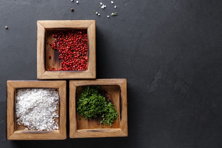 Spices assortment on black background. Salt, peppers and green parsley in wooden boxes on dark background, closeup, copy space, top viewの写真素材