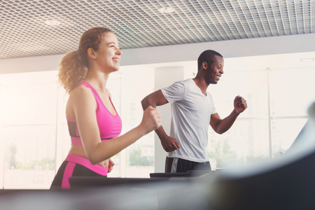 Couple run on treadmills. Man and woman cardio workout in fitness club. Healthy lifestyle, training in gym. Flare effectの写真素材