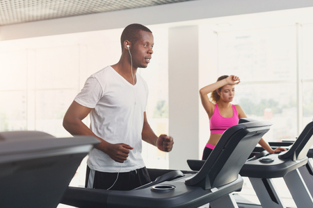 Tired couple run on treadmills. Man and woman cardio workout in fitness club. Healthy lifestyle, training in gym. Flare effectの写真素材