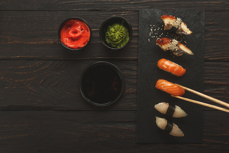 Eating sushi. Japanese food restaurant, unagi and salmon sushi on dark background. Taking piece with chopsticks. Top view on black wood, copy spaceの写真素材