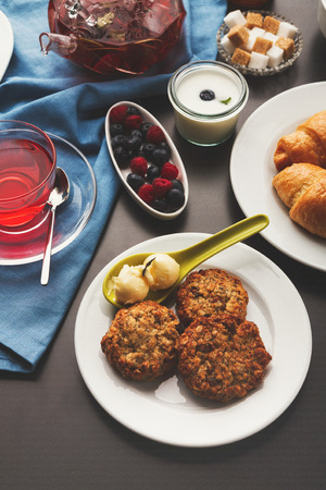 Sweet restaurant breakfast with oatmeal cookies, croissants, yogurt, fresh berries and freshly brewed tea served on black table. Nourishing morning mealsの写真素材
