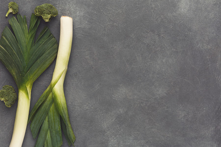Green fresh vegetables border on gray table top view. Harvest background with leek, cucumber, broccoli and pepper. Organic cooking ingredients and healthy eating concept, copy spaceの写真素材