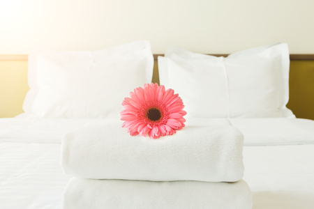 Stack of towels and flower on bed in hotel room. Bright gerbera as welcome gesture, room service, accommodation concept, copy spaceの写真素材