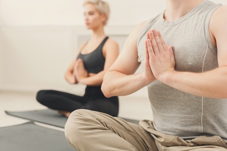 Attractive couple practicing yoga sitting in padmasana. Unrecognizable man and woman in lotus pose, namaste on mat at sport club interior, copy spaceの写真素材