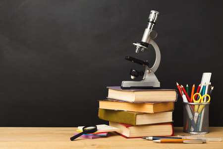 Educational background. Microscope, books pile, pencils and magnifying glass against empty classroom blackboard for copy space. Back to school conceptの写真素材