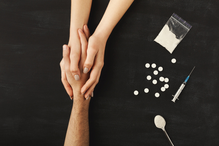Drug addict hands asking for help on dark table with cooked heroine, pills, spoon and plastic bag. Concept for drug addiction and International Day against Drug Abuse, top viewの写真素材