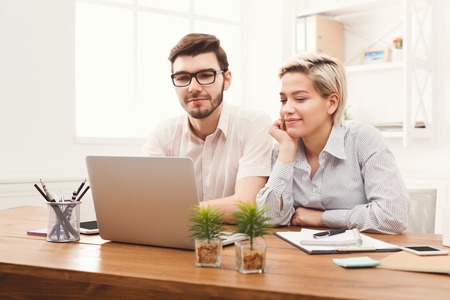 Happy couple of young colleagues working in modern office. Two coworkers working on laptopの写真素材