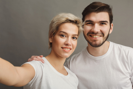 Happy couple together. Love embrace, man and woman taking selfie on smartphone on gray background