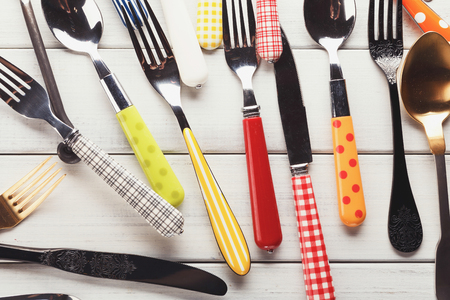 Top view on various forks, knives and spoons. Set of assorted cutlery with fancy handles, flat lay on white rustic wooden planks. Antique and modern kitchenwear backgroundの写真素材