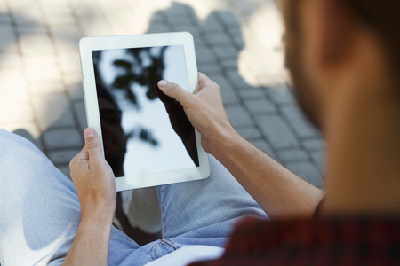 Male hands with tablet closeup, over shoulder shot. Man working outdoors on device with blank screen for copy space. Technology, communication, education and remote working concept.の写真素材