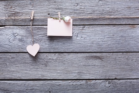 Valentine background with light pink paper heart and empty greeting card and rose on clothespins on rustic wood planks, copy space. Valentine's Day, love, romantic concept. Horizontal orientationの写真素材