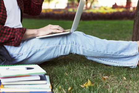 Young casual man with laptop outdoors. Unrecognizable male student preparing for exams with computer and books in park. Education and entering university concept, crop, copy space.の写真素材