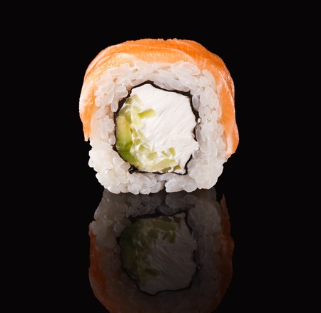 Sushi roll with fish, vegetables and cheese. Traditional japanese food on black glass with reflection, copy space. Asian restaurant meals deliveryの写真素材