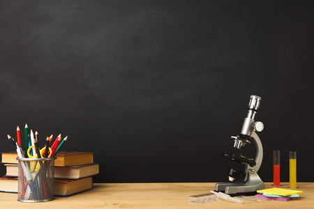 Educational background. Microscope, books pile, pencils and magnifying glass against empty classroom blackboard for copy space. Back to school conceptの写真素材