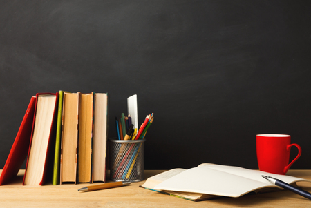 Educational background. Books, pencils, coffee cup and open notebook against empty classroom blackboard for copy space. Back to school conceptの写真素材