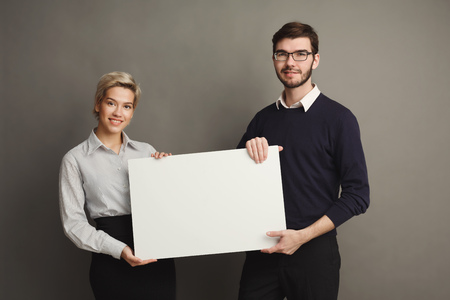 Happy young couple holding blank white banner with copy space on gray backgroundの写真素材