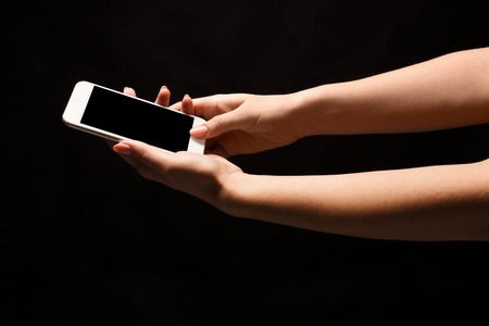 Female hand holding mobile smartphone with blank screen, isolated on black background. Copy space...