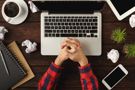 Mans hands on laptop. Top view of human hands, laptop keyboard, coffee, notebook and crumpled paper on brown wooden table background. Education, business, technology conceptの写真素材