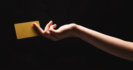 Female hand holding blank plastic credit card or business card on black isolated studio background. Banking services and acquaintance concept, copy space, cutout, low keyの写真素材