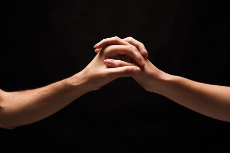 Male and female hands holding tight together on black isolated background. Love, relations, support, together forever concept. Copy space, cutout, low keyの写真素材