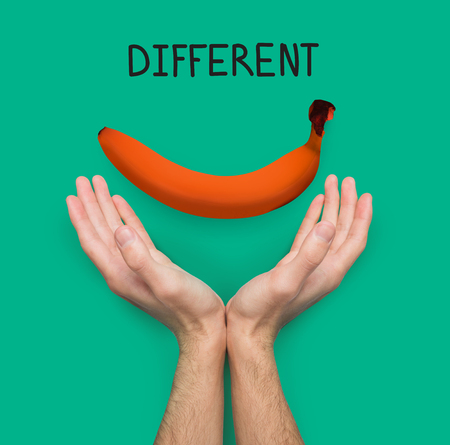 Conceptual lifestyle background. Male hands against backdrop with orange colored banana and different inscription. Dare to be different and individuality motivation posterの写真素材