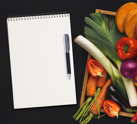 Mockup for healthy dish recipe. Fresh juicy vegetables border, blank white notepad with copy space and pen on black background, top view.の写真素材