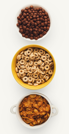 Variety of cold quick breakfast cereals isolated on white. Set of bowls with corn balls, rings and flakes. Morning meals for children collection, top view, cutoutの写真素材
