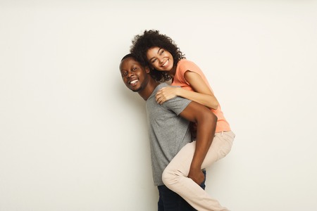 Loving black couple piggybacking. Happy young man with his girlfriend, white isolated studio background, copy spaceの写真素材