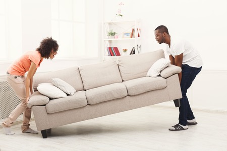 Full length of happy black couple placing sofa in living room of new home. Moving, interior design...