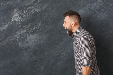 Man cry out in despair and shock. Expressing strong emotions, anger at grey background, studio shot, side viewの写真素材