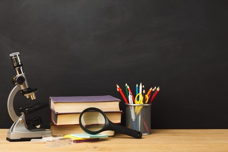 Educational background. Microscope, books pile, pencils and magnifying glass against empty classroom...