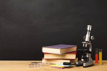Educational background. Microscope, books pile, pencils and magnifying glass against empty classroom blackboard for copy space. Back to school conceptの写真素材
