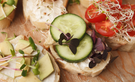 Healthy sandwiches with creamy cheese, avocado, cucumber, cherry tomatoes and micro greens on rustic wooden board. Vegetarian snackの写真素材