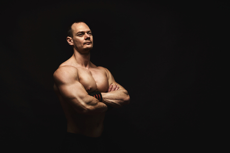 Strong athletic man, bodybuilder. Naked torso, muscular body. Strong chest and shoulder muscles. Studio shot on black background, low key. Bodybuilding conceptの写真素材
