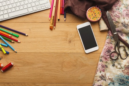Fashion designer workspace top view. Sewing equipment, colored pencils, laptop and mobile on wooden table with copy spaceの写真素材
