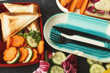 Healthy food concept. Lunch box filled with mixed vegetables, toasted sandwiches and cutlery. Closeup of various snacks for school dinnerの写真素材