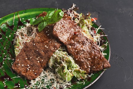 Small pork steaks with fresh vegetable salad on black background. Fried meat served with garnish, copy spaceの写真素材