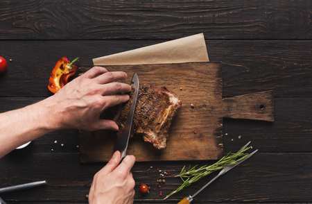 Hand cutting grilled meat on rustic wooden board. Preparing for serving fried steak, top view, copy spaceの写真素材