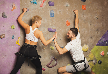 Happy man and woman fitness professional climbers having training at bouldering gym. Young sportsmen climbing artificial rock wall, reaching the top and support conceptの写真素材