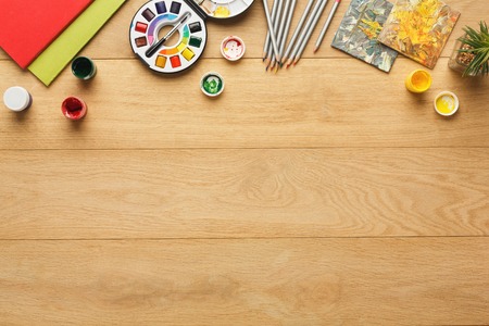 Border of various stationery for art, top view. Light wooden desktop with pencils, colors, paper. Studying and creative background, copy spaceの写真素材