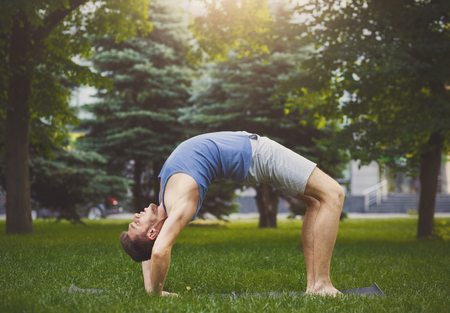 Fitness, man training yoga in table top pose on green grass in park. Young guy makes aerobics exercise outdoors, copy spaceの写真素材